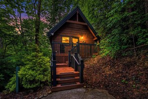 Una cabaña con una escalera que lleva a una terraza, rodeada de un bosque denso.