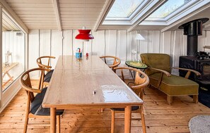 Ein Holztisch mit Stühlen, eine rote Pendelleuchte, ein grüner Sessel und ein Kaminofen.
