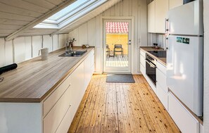 Eine kleine Küche mit Holzausziehtisch, Spüle, Kühlschrank und einem durch eine Tür erreichbaren Essbereich.