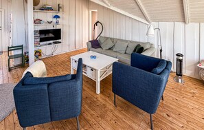Ein gemütliches Wohnzimmer mit einer Couch, zwei Sesseln, einem Couchtisch, einem Fernseher und einem Bücherregal.