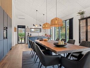 Eine moderne Küche mit Kochinsel, Pendelleuchten und einem Essbereich mit langem Tisch und Stühlen.