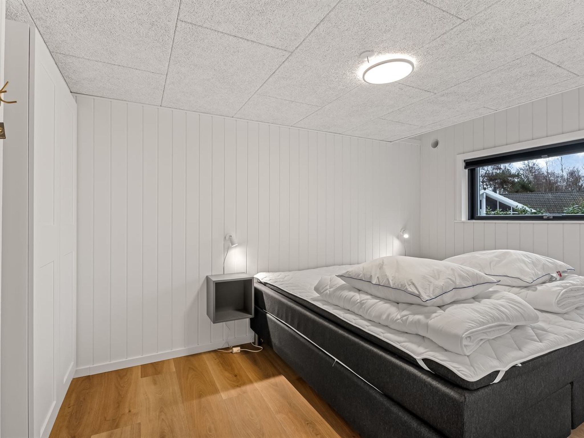 Une chambre à coucher avec un lit, des tables de chevet, une fenêtre et un luminaire au plafond.