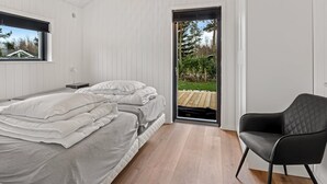 Ein Schlafzimmer mit einem Bett, einem Sessel, einem Fenster und einer Tür, die zu einem Außenbereich führt.