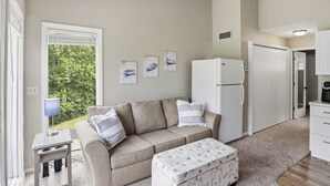 A cozy living room with a sofa, ottoman, and a refrigerator. - Reel Sweet Perch - Indoor Pool, Lakeside Pool, & Hot Tub! (Village of Four Seasons)