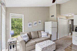 Ein gemütliches Wohnzimmer mit einer Couch, einem Hocker und einem Kühlschrank.