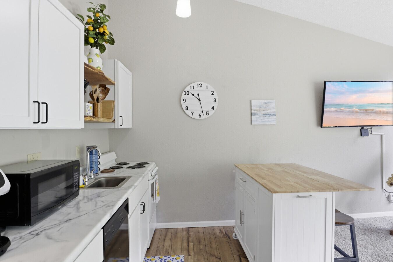 Une cuisine compacte avec des meubles blancs, un four à micro-ondes, une cuisinière et une petite table en bois.