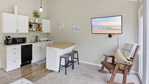A modern kitchen with white cabinets, a microwave, and a coffee maker. There is a wooden island with stools, a clock, and a TV displaying a beach scene. - Reel Sweet Perch - Indoor Pool, Lakeside Pool, & Hot Tub! (Village of Four Seasons)