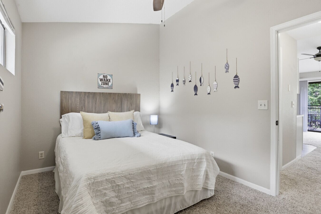 A bedroom with a bed, a headboard, a wall-mounted fish decoration, and a door leading to another room.