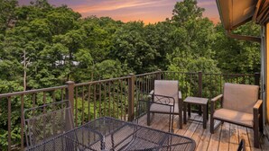 A balcony with outdoor furniture, a metal table, and a view of dense trees. - Reel Sweet Perch - Indoor Pool, Lakeside Pool, & Hot Tub! (Village of Four Seasons)