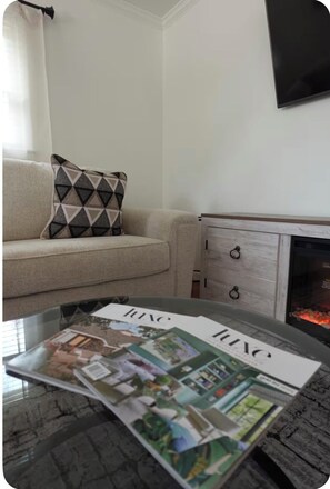 A living room with a sofa, a patterned pillow, a magazine on a coffee table, a fireplace, and a TV mounted on the wall. - Relaxing 3BR Near RAFB with AC & WiFi (Warner Robins)
