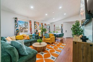 A modern living room with a sofa, coffee table, and a dining area with chairs. - 5BR Movie Theater, Hot Tub, Mini Golf, Game Room! (McGaheysville)