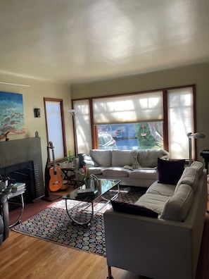 Ein Wohnzimmer mit Kamin, einer Couch, einem Couchtisch, einer Gitarre und Blick ins Freie.