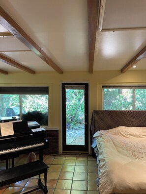 Ein Zimmer mit Klavier, einem Bett und einer Tür zu einem Garten.