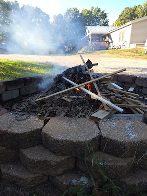 A campfire with logs and a metal fire pit surrounded by a stone wall.