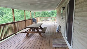 A covered deck with a picnic table, a grill, and a door leading to a house.