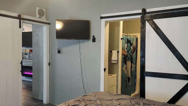 A bedroom with a bed, a ceiling fan, a TV, and a sliding door leading to a bathroom.