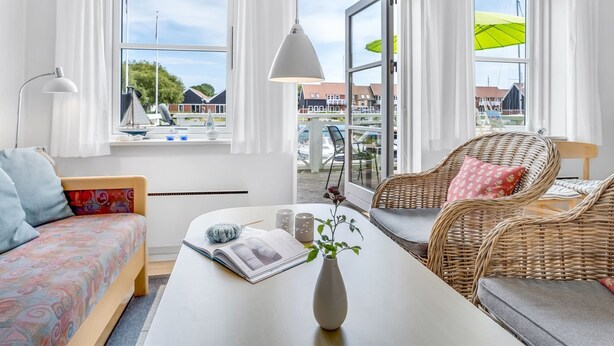 A bright room with a sofa, a wicker chair, a table with a book and a vase, and large windows with curtains. - "Thorfin" - 10m from the sea by Interhome (Borre)