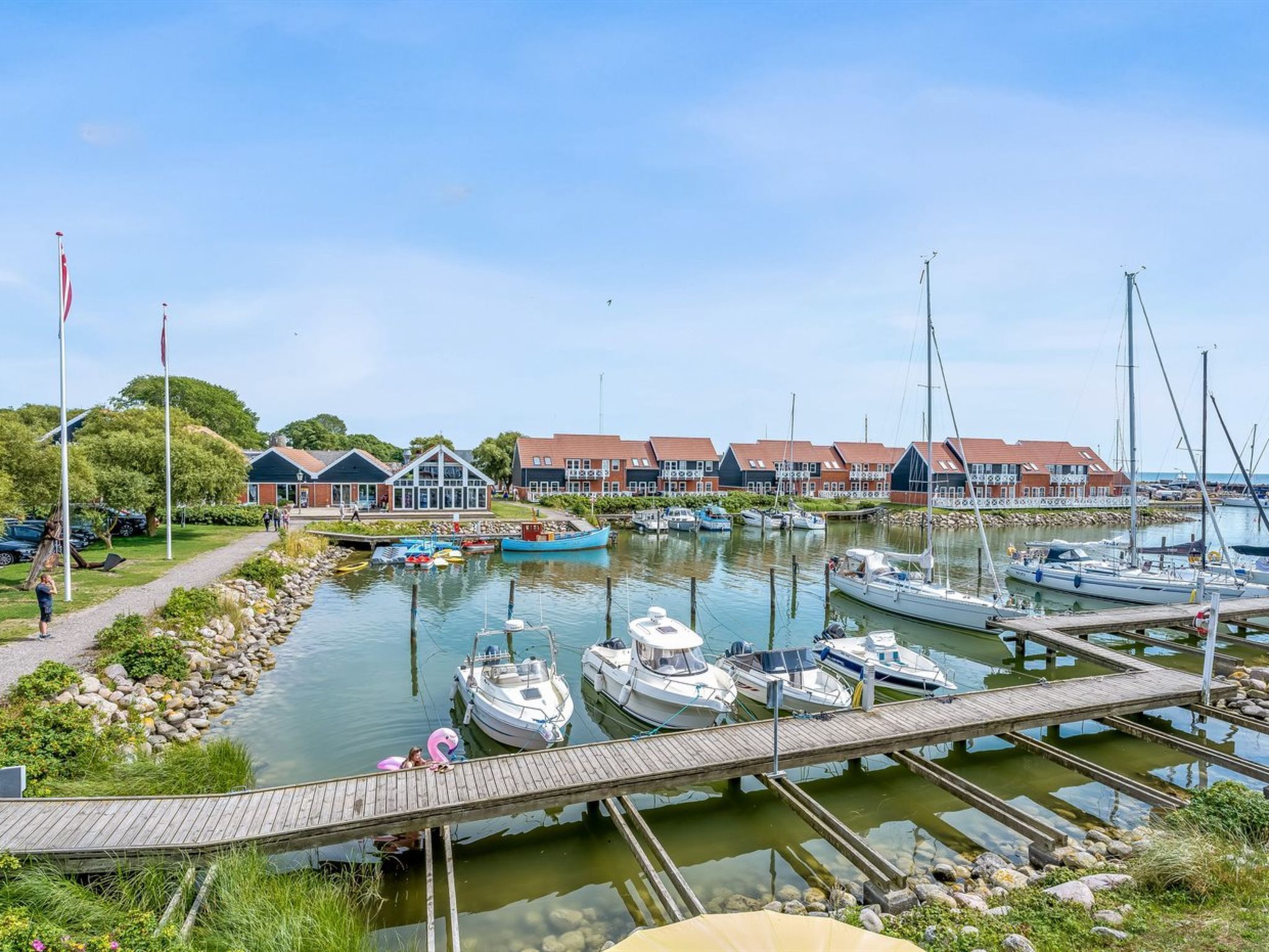 A marina with boats docked, a wooden pier, and row houses in the background.