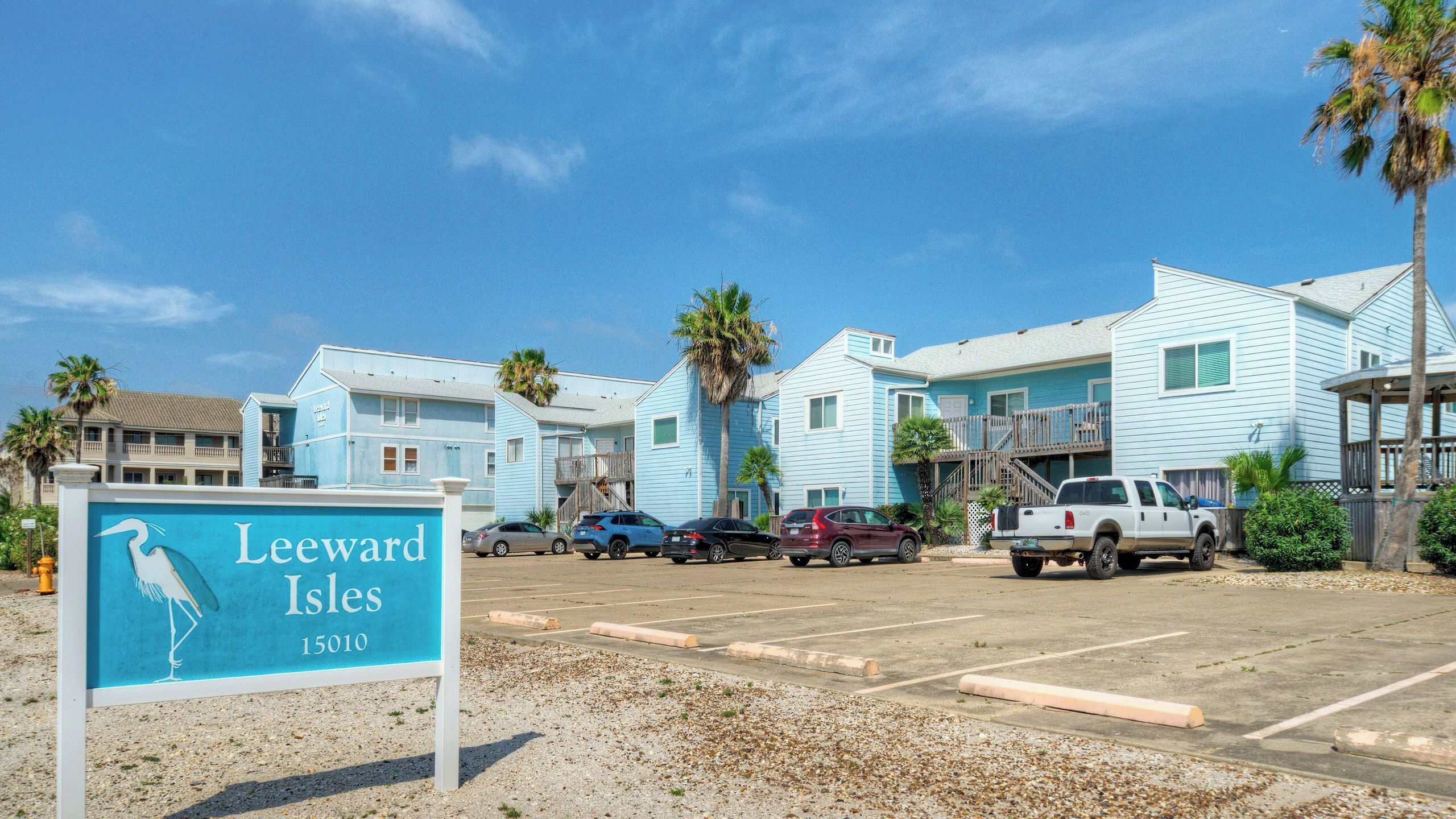 A beachfront property with a parking lot, several vehicles, and a sign indicating 'Leeward Isles 15010'.