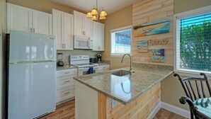 A kitchen with white cabinets, a built-in microwave, a granite countertop, a sink, and a window with blinds. - Sea Gypsy by Avantstay 1BR Coastal Condo + Shared Pool Short Walk to Beach + Mins to Port A (Corpus Christi)