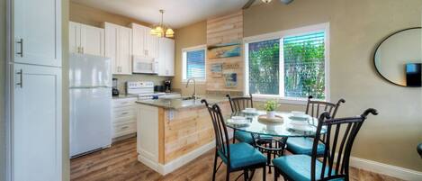 A kitchen with white cabinets, a central island, and a dining area with blue chairs.