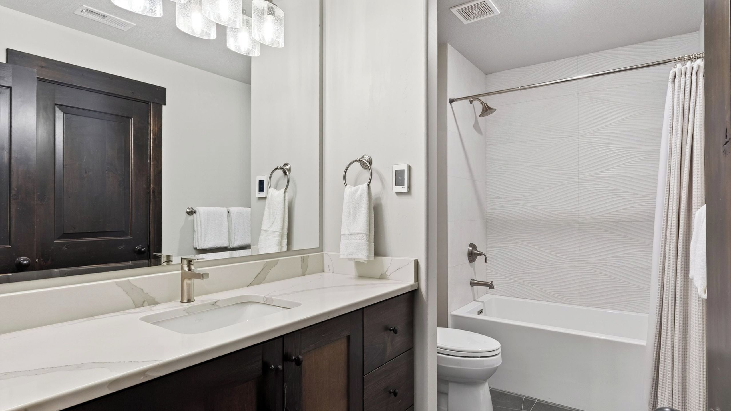 A modern bathroom with a large mirror, two sinks, a toilet, and a shower.