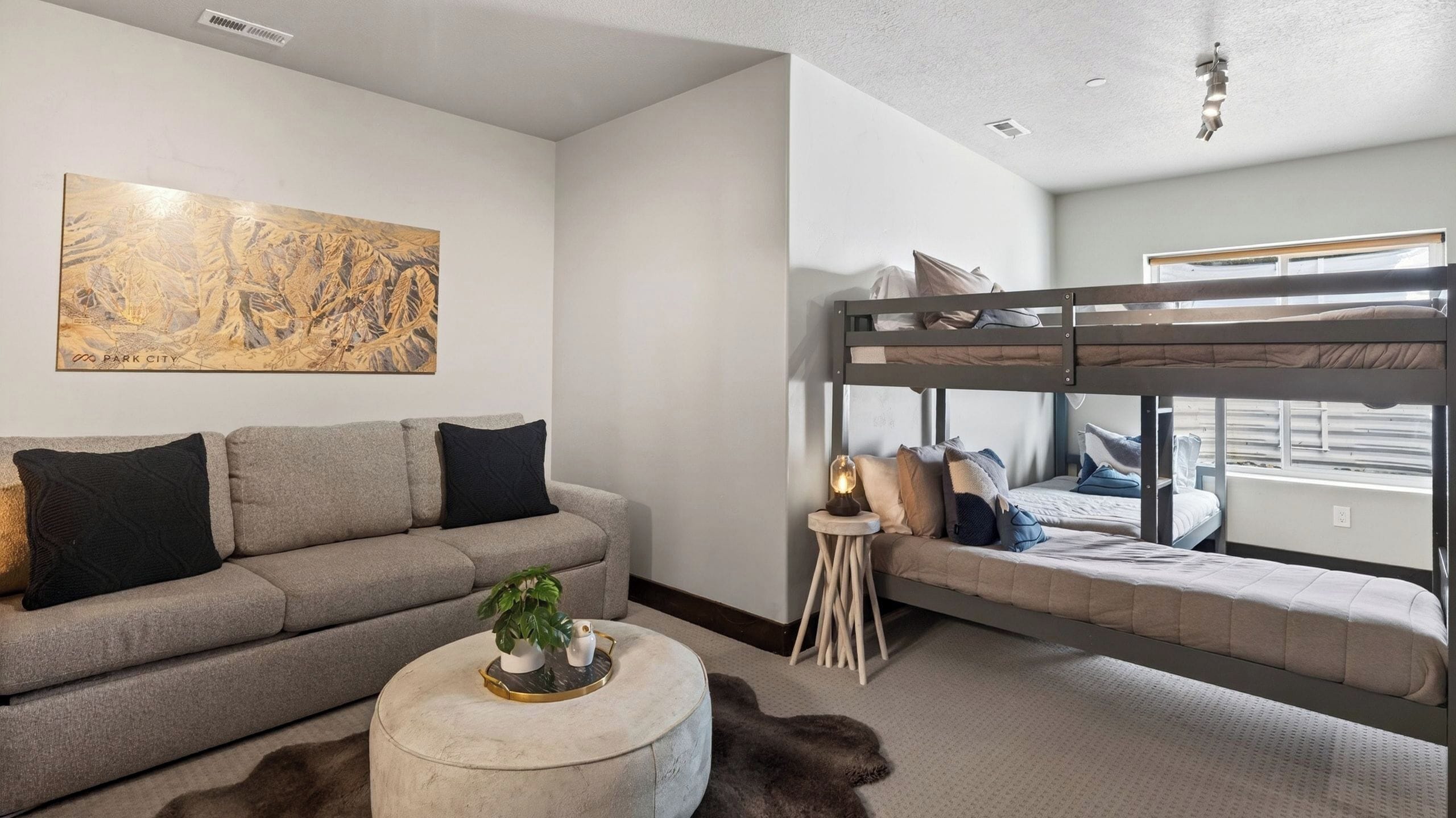 Una habitación moderna con un sofá, una mesa redonda con una planta, una cama litera y un cuadro abstracto grande en la pared.