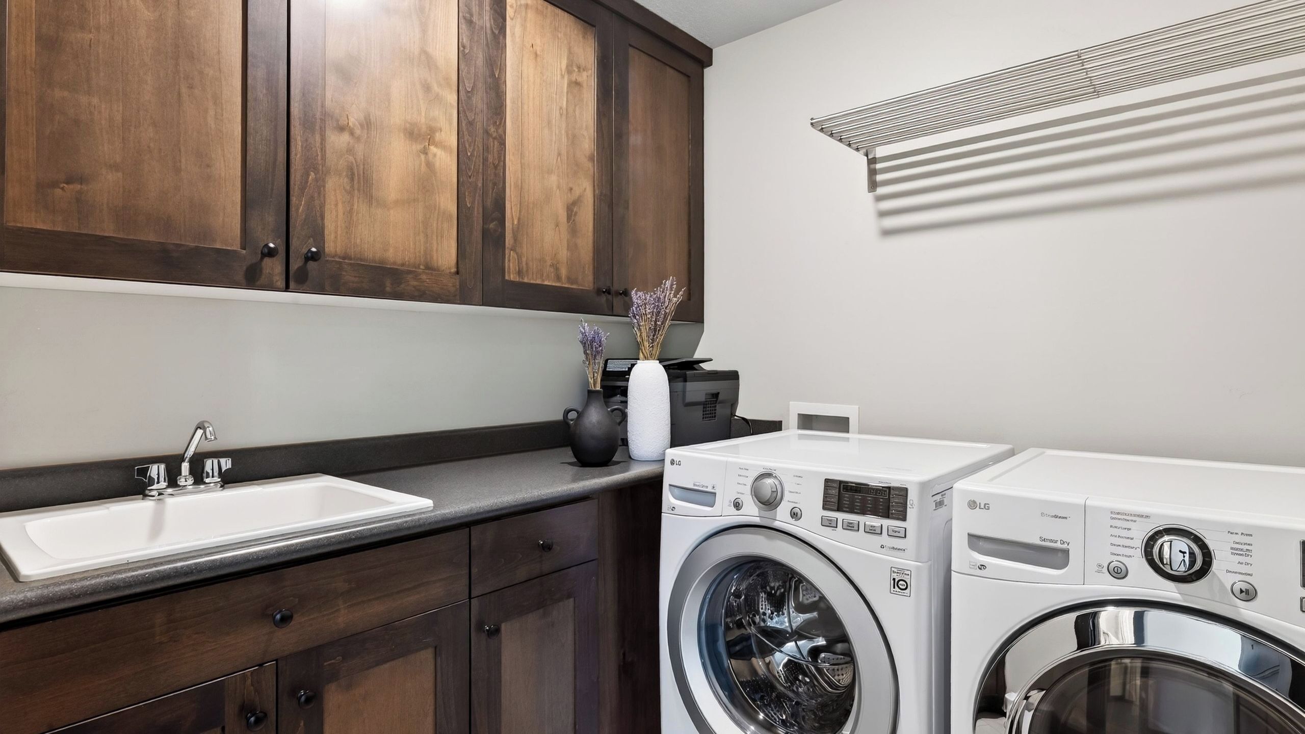 Un cuarto de lavandería con lavadora, secadora, lavabo y armarios de madera oscura.