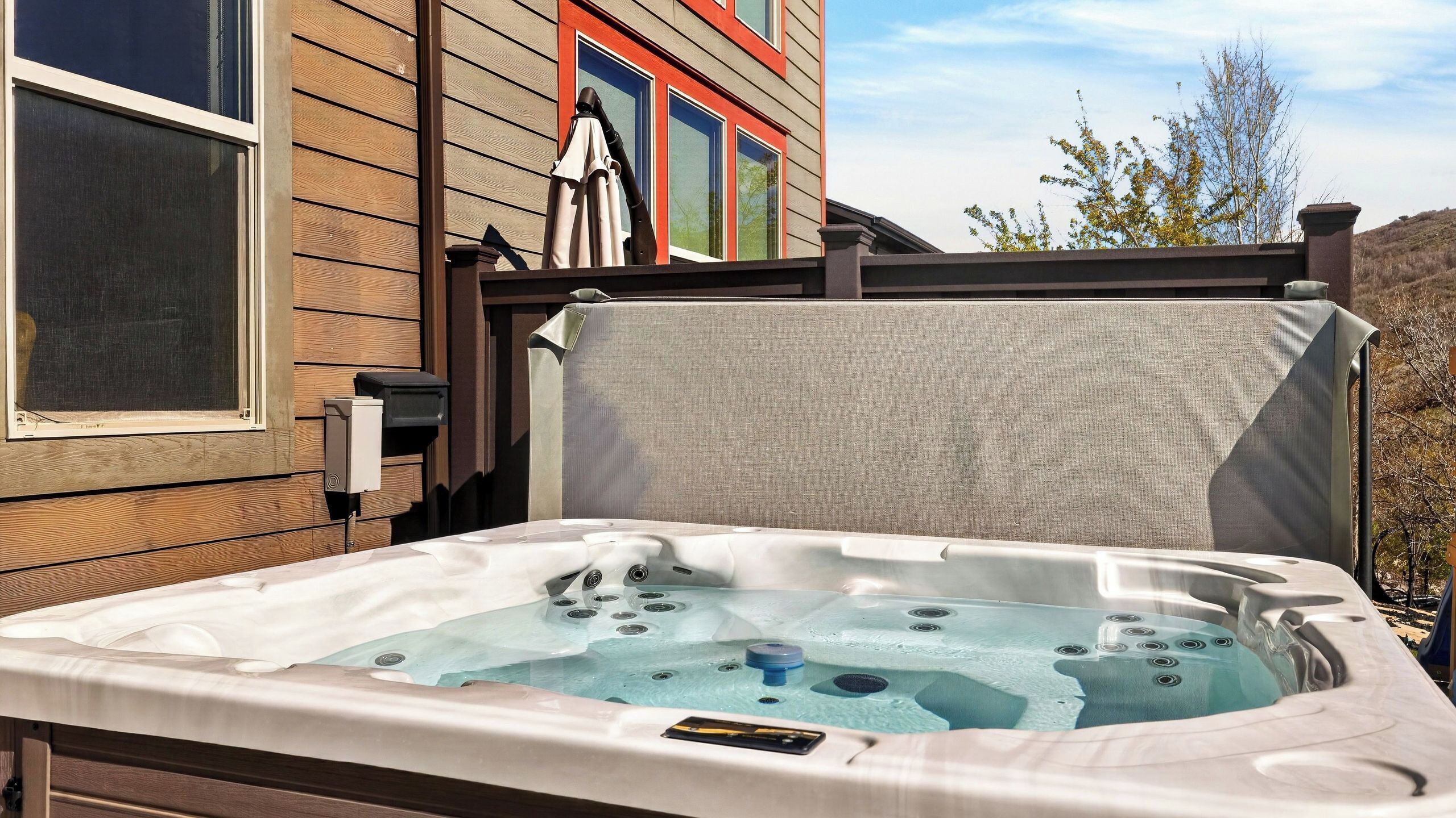 A hot tub in front of a house with a wooden exterior and a window.