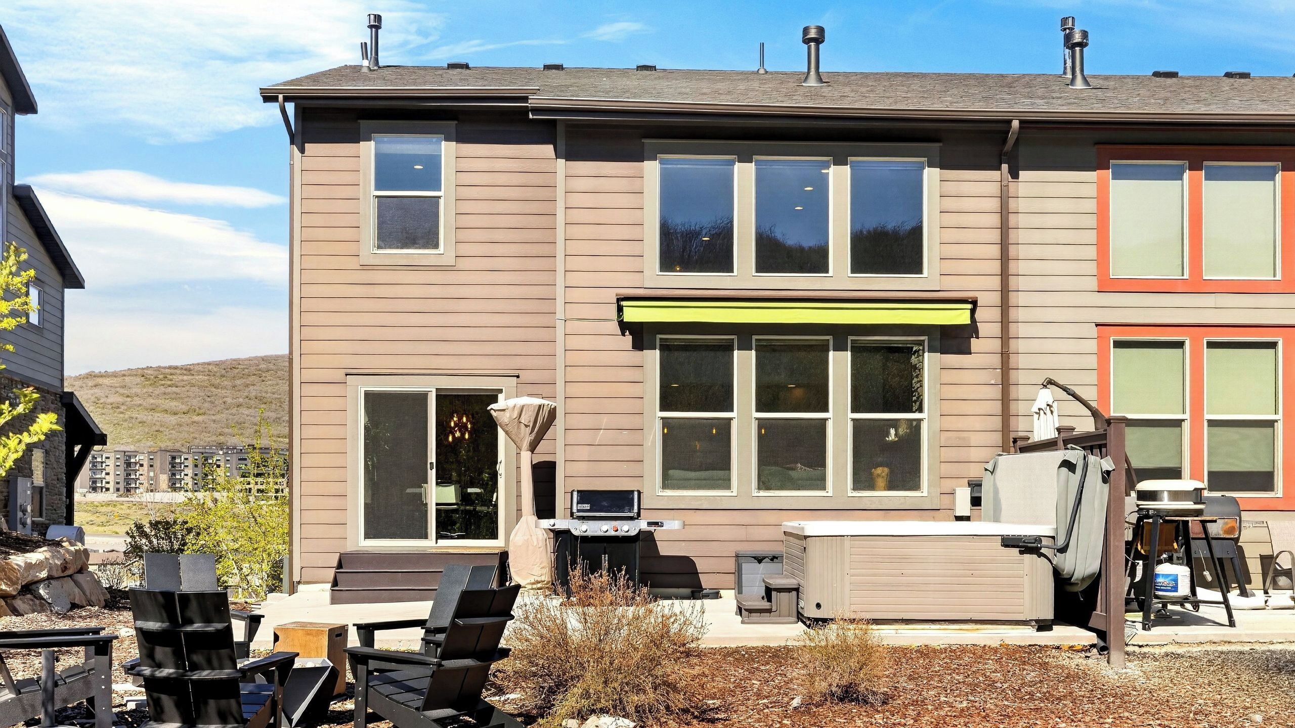 A two-story house with a patio area, outdoor furniture, and a grill.