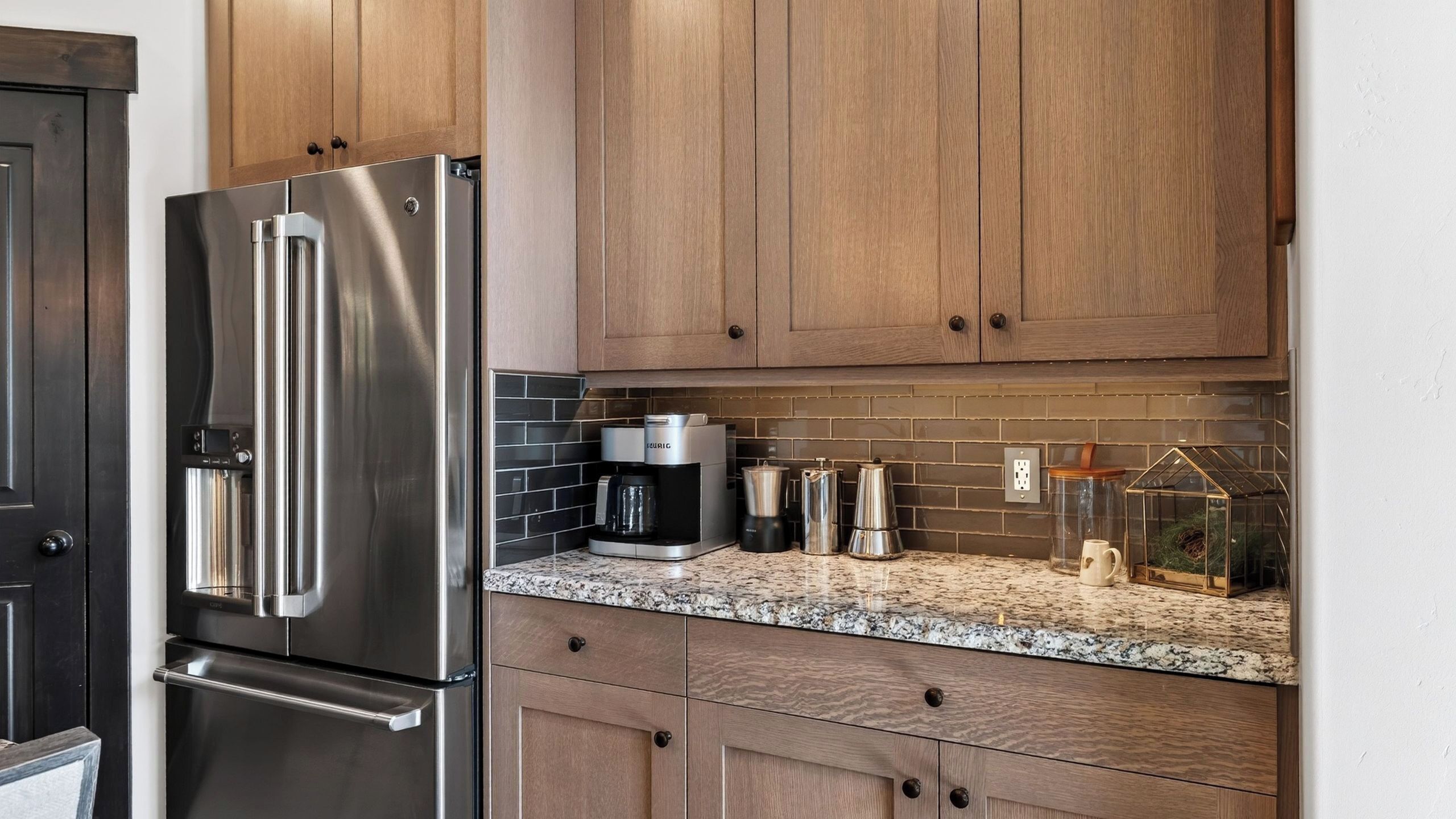 A kitchen with stainless steel appliances, wooden cabinets, a coffee maker, and a glass container on the countertop.