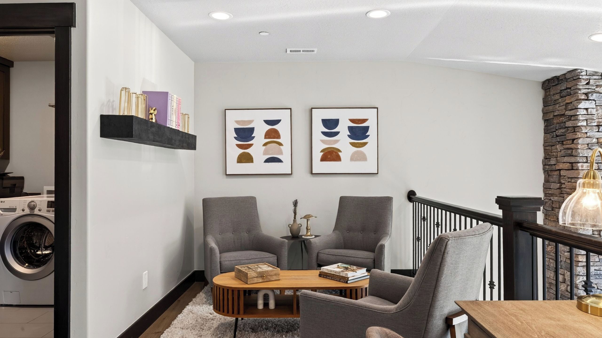 Un salon moderne avec deux fauteuils gris, une table basse en bois et deux tableaux abstraits accrochés au mur.