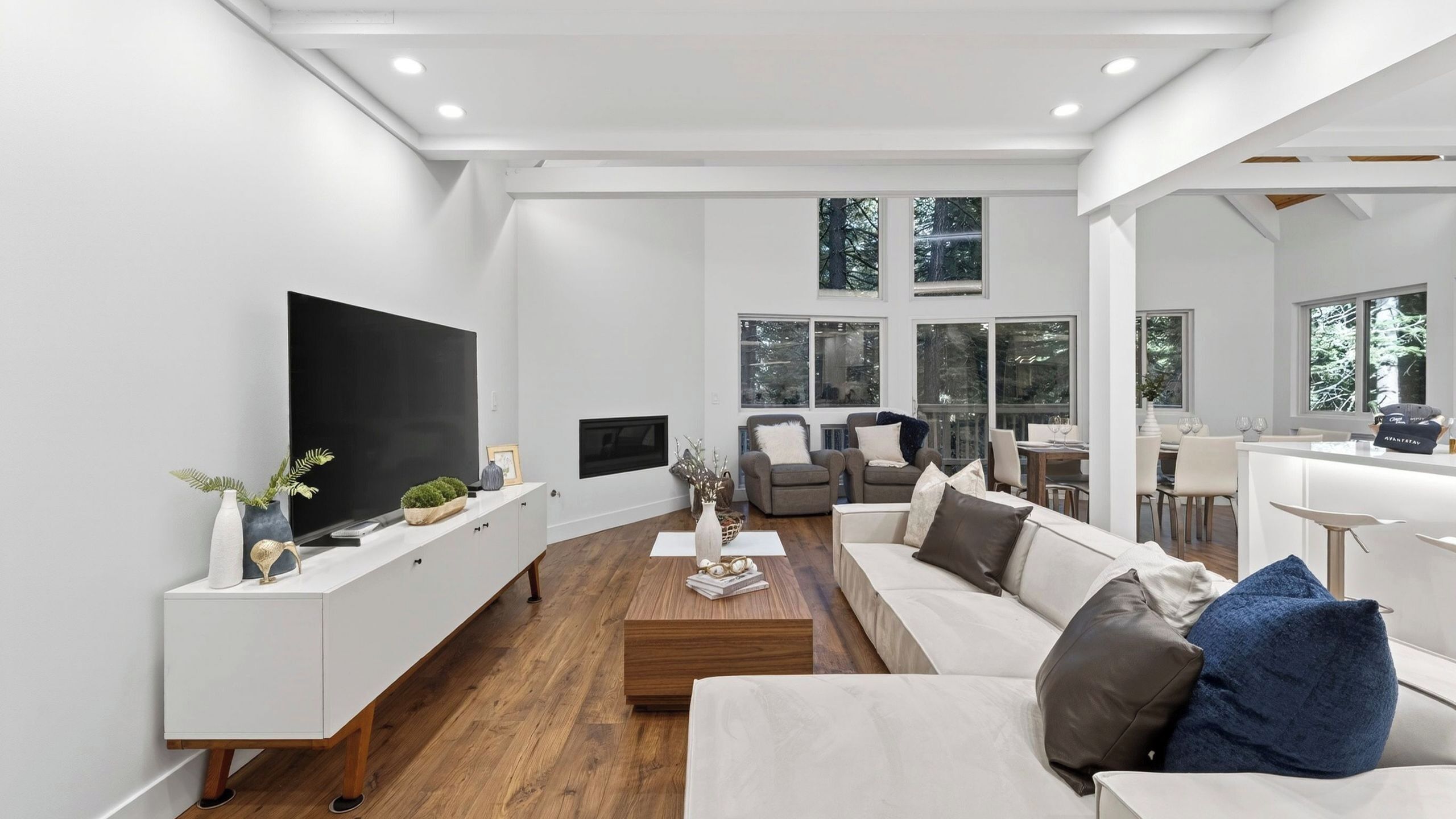 A modern living room with a large flat-screen TV, a sofa, a coffee table, and a dining area with a bar.