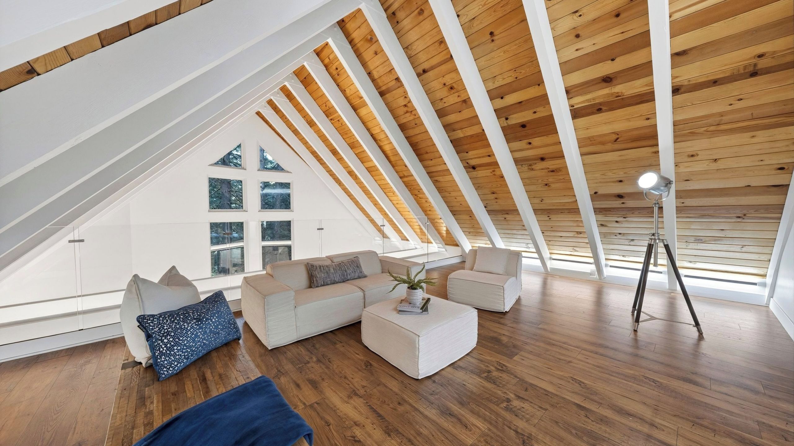 Un loft moderno con soffitto spiovente, travi in legno, un divano bianco, un tavolino da caffè e una lampada da terra.
