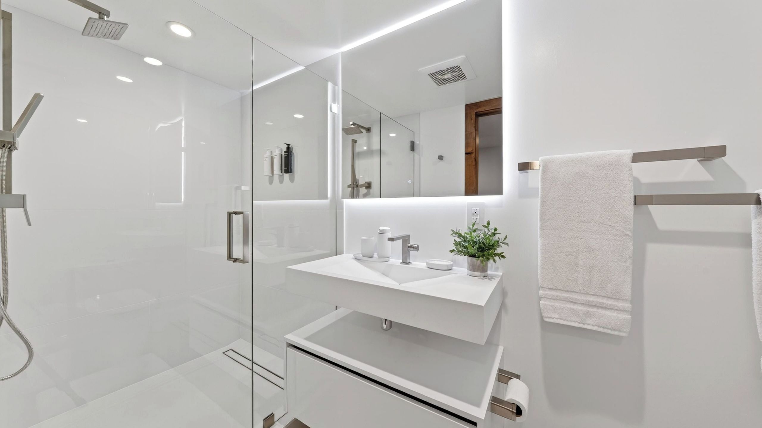 A modern bathroom with a glass shower enclosure, a white sink with a mirror above, and a towel rack.