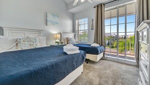 Een slaapkamer met twee bedden, een plafondventilator, een groot raam met gordijnen en uitzicht op de omgeving.