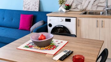 Une cuisine compacte équipée d’un lave-linge, d’un évier et d’un canapé bleu.