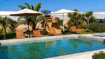 A swimming pool with clear water, surrounded by wooden lounge chairs and umbrellas.