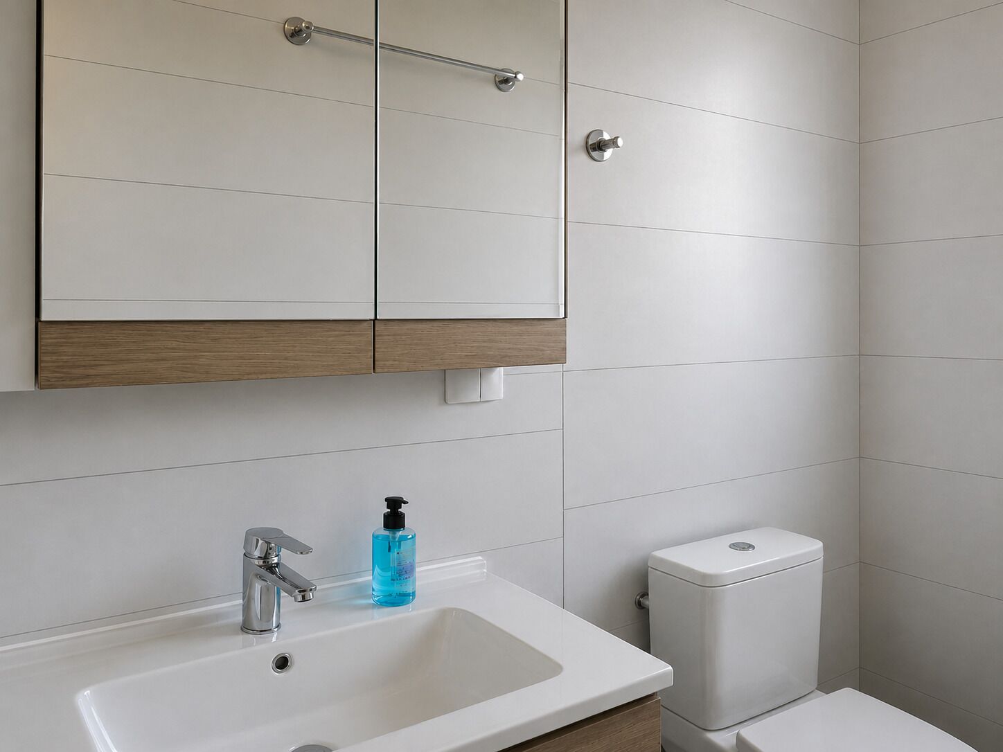 A bathroom with a white sink, a mirror, a toilet, and a wooden cabinet.