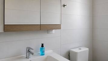 A bathroom with a white sink, a mirror, a toilet, and a wooden cabinet.