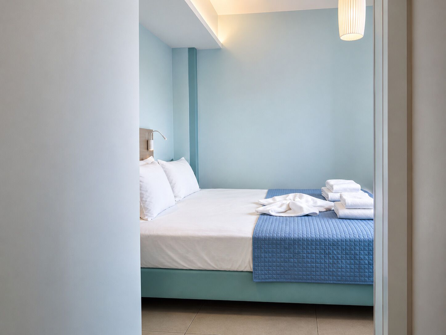 A neatly made bed with white and blue bedding, a bedside lamp, and a stack of white towels.