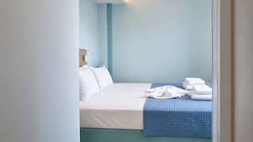 A neatly made bed with white and blue bedding, a bedside lamp, and a stack of white towels.