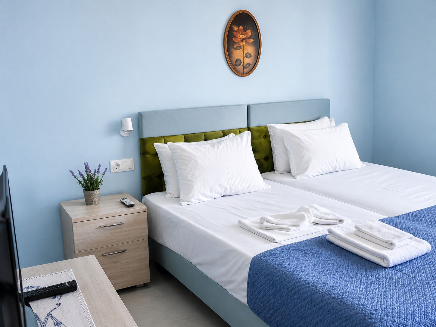 A hotel room with a bed, bedside table, lamp, and a wall-mounted painting.