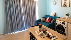 Ein kompakter Wohnraum mit Esstisch, Waschmaschine, blauem Sofa und einer Wandleuchte.
