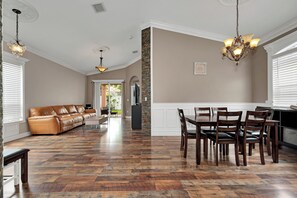 Amplia sala de estar con sofá de cuero, mesa de comedor con sillas y zona de cocina con un muro decorativo de piedra.