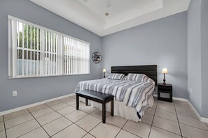 Un dormitorio con una cama, un banco, una mesita de noche, un reloj de pared y una ventana con persianas.