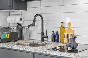 A kitchen with a stainless steel sink, a dish soap dispenser, a hand soap dispenser, a bottle of olive oil, a wooden cutting board, and a salt and pepper shaker. - Central Studio Haven | Pool, Gym & View Decks Area (Houston)