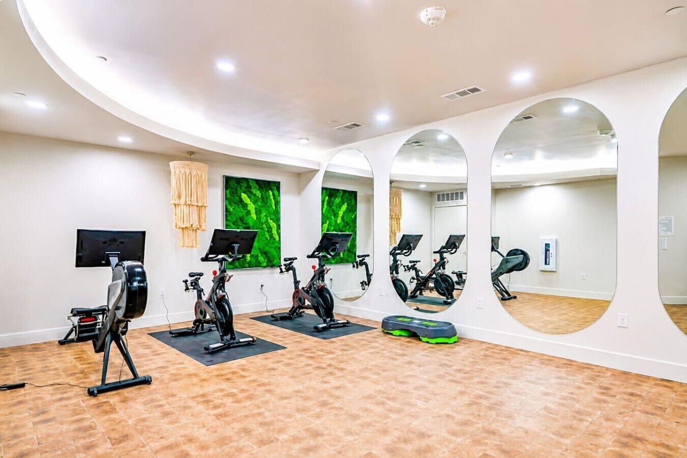 A gym with exercise bikes, mirrors, a TV, and a wooden floor.