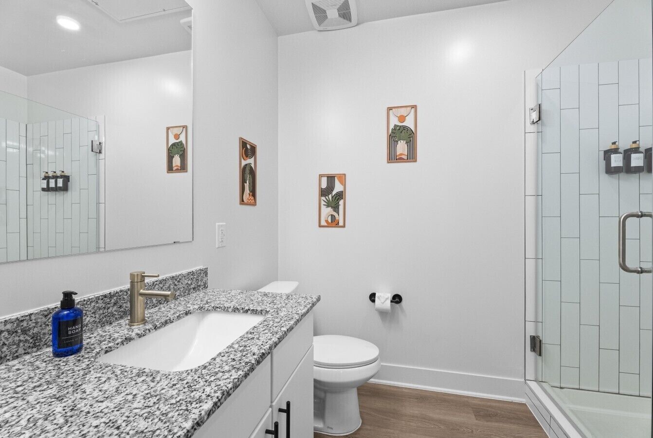 A modern bathroom with a granite countertop, a white toilet, and a glass shower enclosure.
