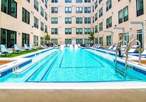 Ein Schwimmbecken mit mehreren Bahnen, Liegestühlen und einem Gebäude mit großen Fenstern im Hintergrund.
